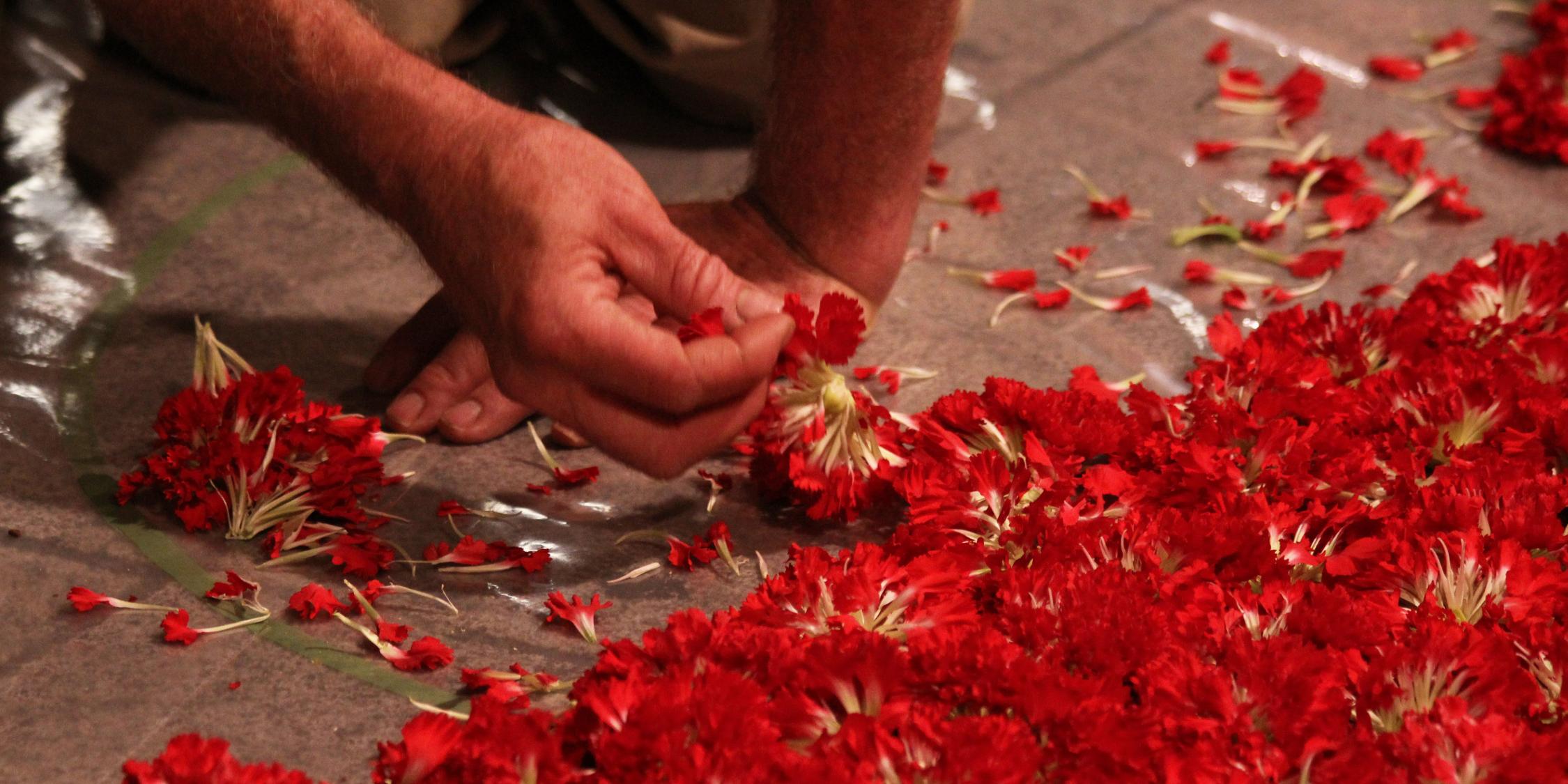 Hand legt rote Nelkenblüten auf den Boden. (c) Bild: „Corpus Christi Puenteareas 2011“ by Elentir / CC-by-sa 2.0 / Quelle: flickr.com In: Pfarrbriefservice.de Hand legt rote Nelkenblüten auf den Boden.
