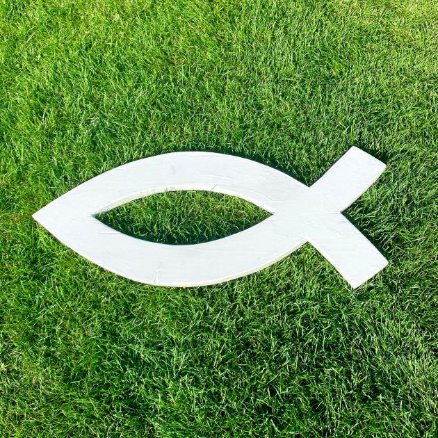 Ein weißes christliches Fischsymbol, Ichthys, liegt auf leuchtend grünem, kurzgeschnittenem Rasen.